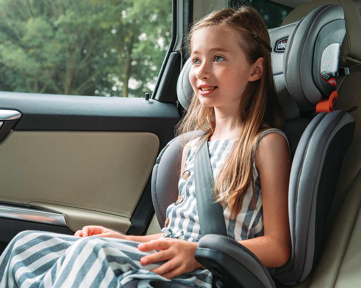 Child seated in a Chicco booster car seat with vehicle seat belt properly positioned
