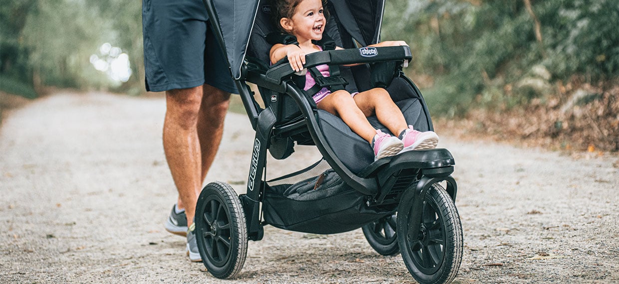 An adult pushing a child in a Chicco jogging stroller on a gravel path