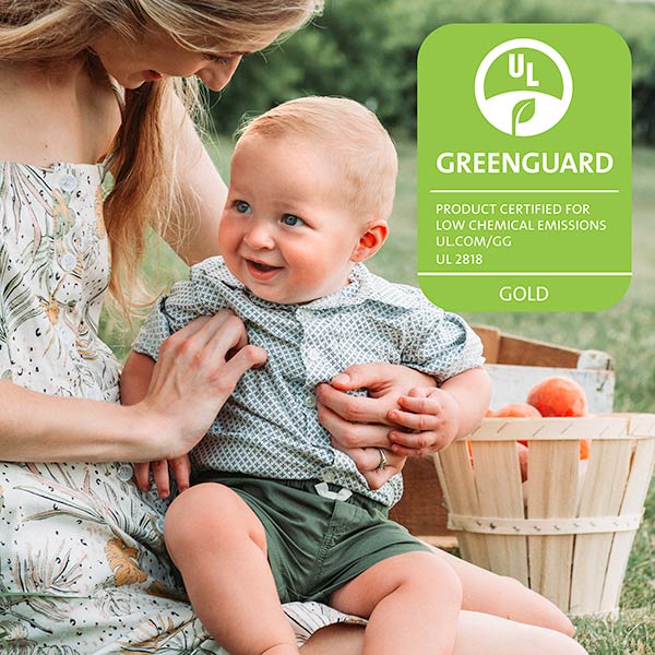Mother holding baby beside a Chicco GREENGUARD Gold Certified car seat icon indicating low chemical emissions.