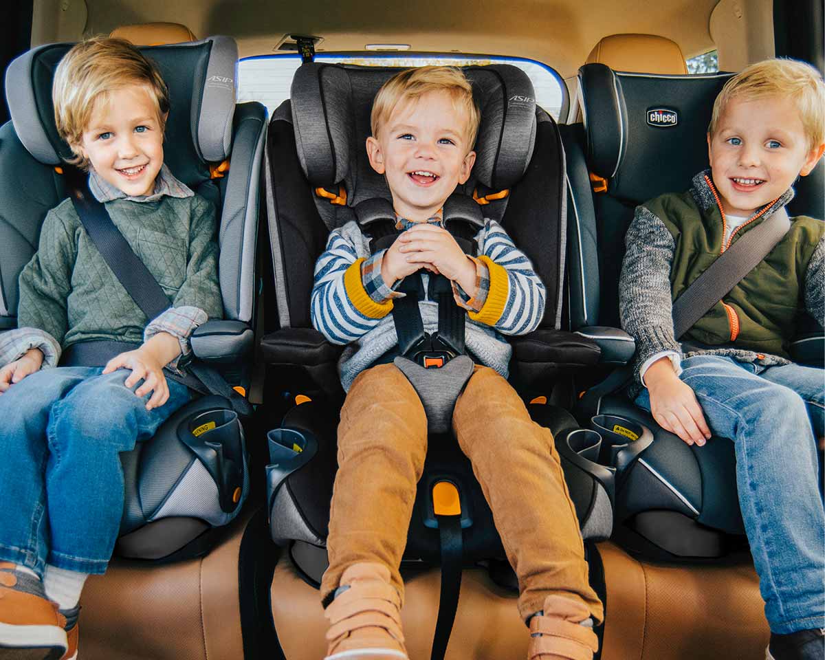 Three children seated in Chicco car seats inside a vehicle